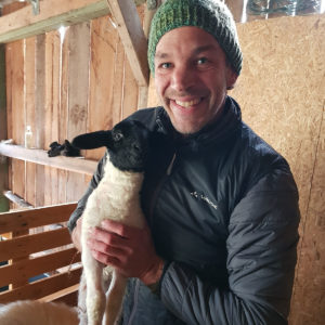 Unternehmercoach Jens Schenk hält eines seiner vielen Schafe auf dem Arm