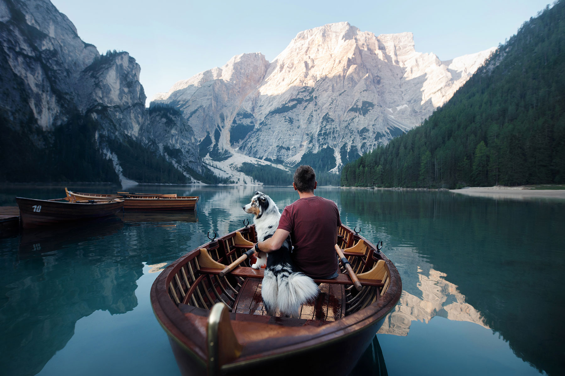 mann mit hund im ruder-boot auf see mit bergen drumherum