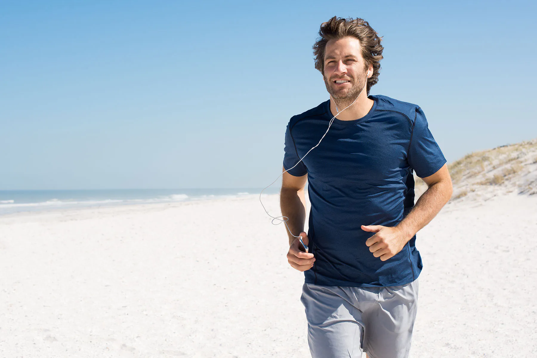 glueklicher mann beim joggen am strand mit kopfhoerern